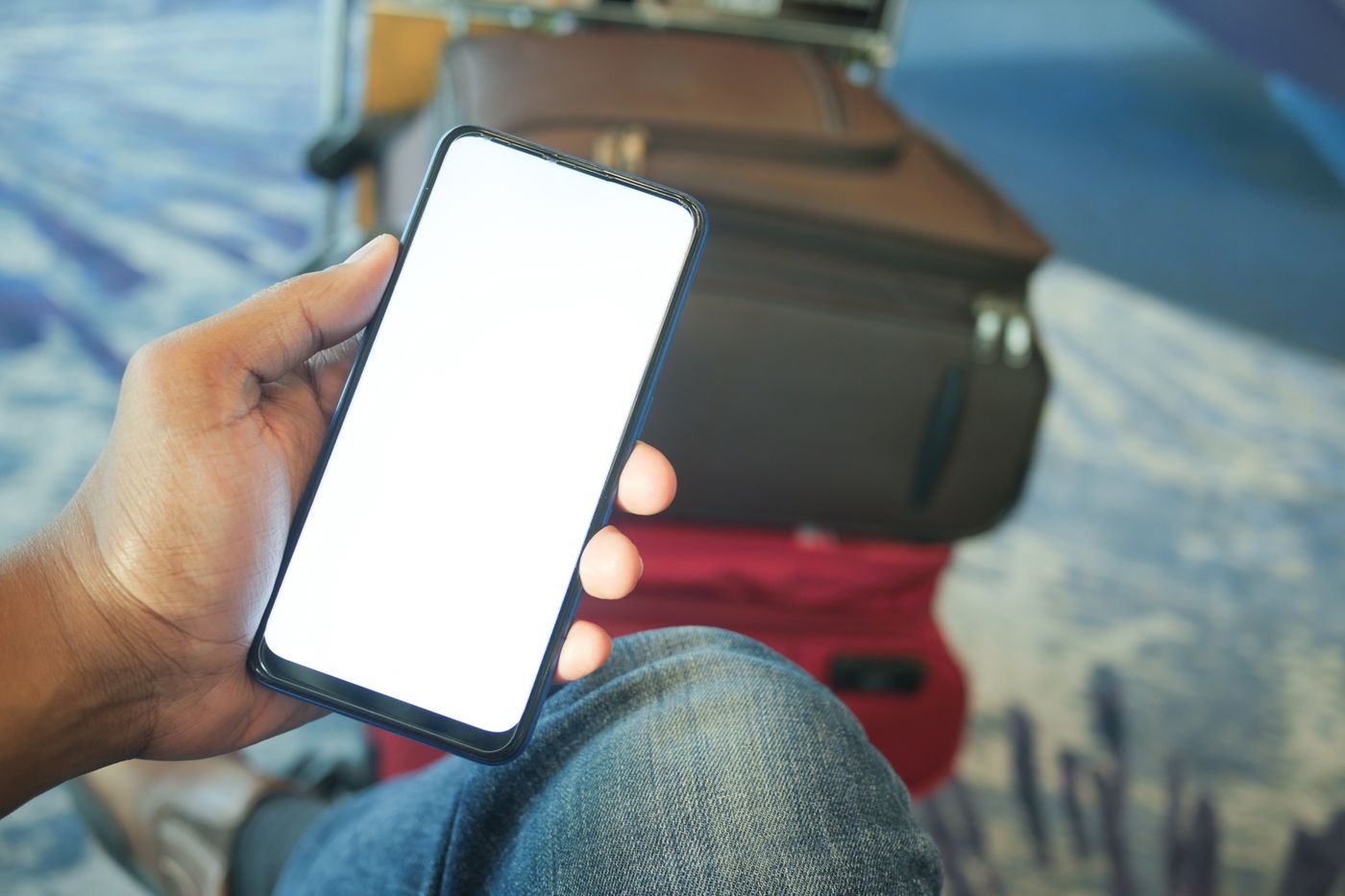 A traveller holds a smartphone in an airport terminal, with suitcases in the background