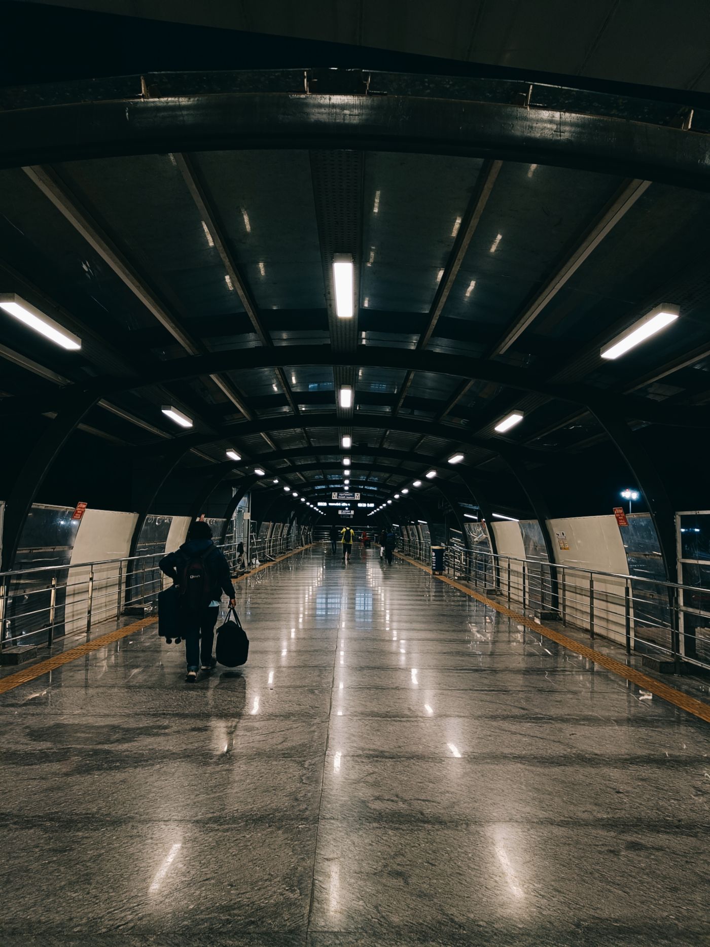 A long, brightly lit airport terminal corridor at night with a traveller pulling a suitcase