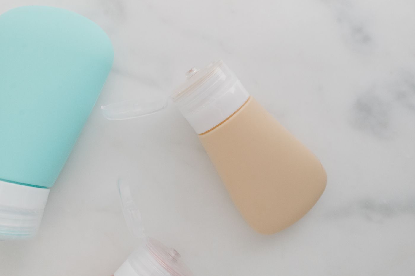 Small refillable travel bottles with flip-top caps on a marble surface