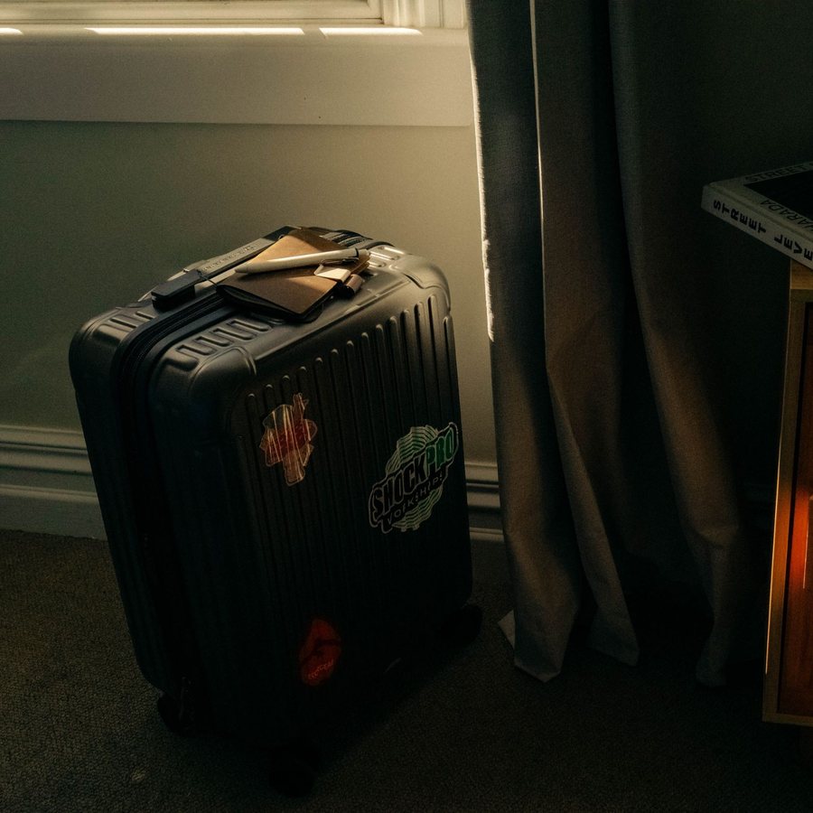 A packed carry-on suitcase with a notebook and pen on top, next to a window